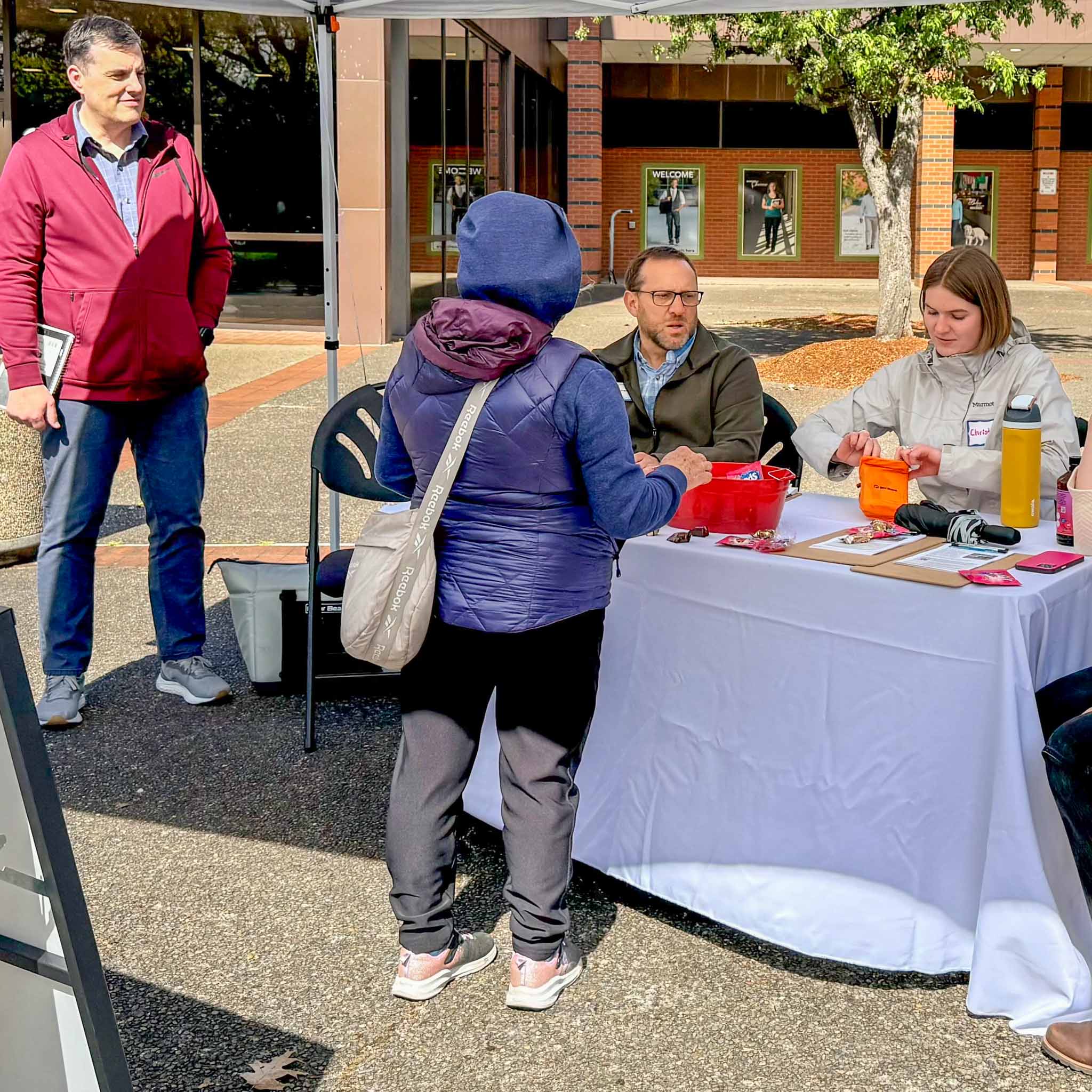 A community member wearing a hooded sweatshirt speaks to four Cherriots representatives at a tabling event at the Chemeketa Community College Transit Center. 